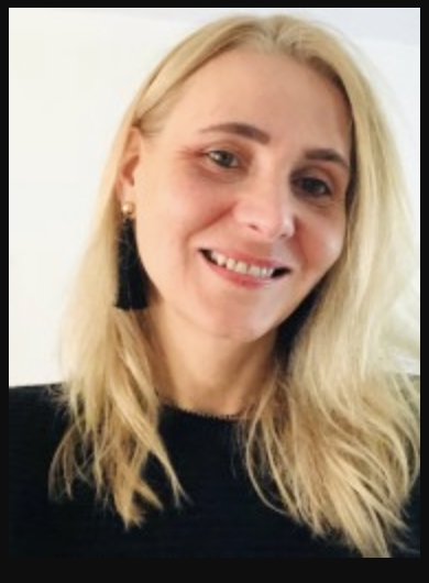 Image of a woman wearing a black shirt, long black earrings, and sporting a smile.