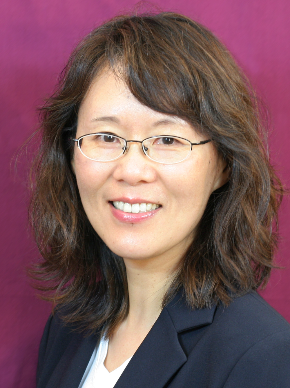 Woman of Asian descent with shoulder-length brown hair, glasses, and a navy blue blazer