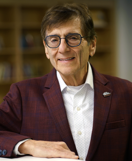 older gentleman with short brown hair, glasses, wearing a burgundy jacket