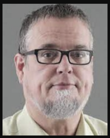 man with short dark hair, grey beard, and black rectangular glasses