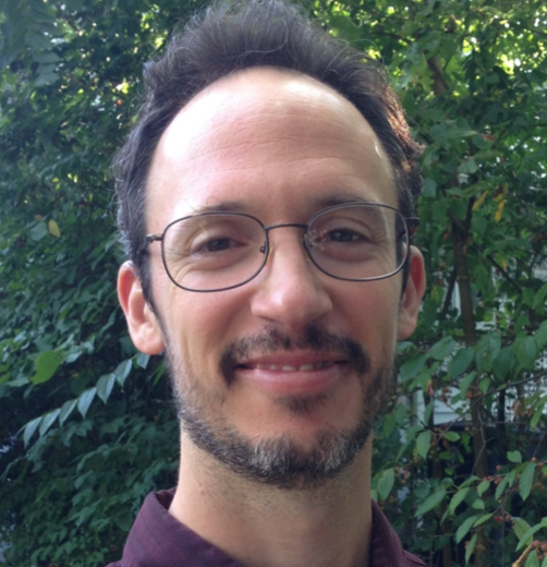 Man smiling with short dark hair, glasses, and a salt a pepper goatee