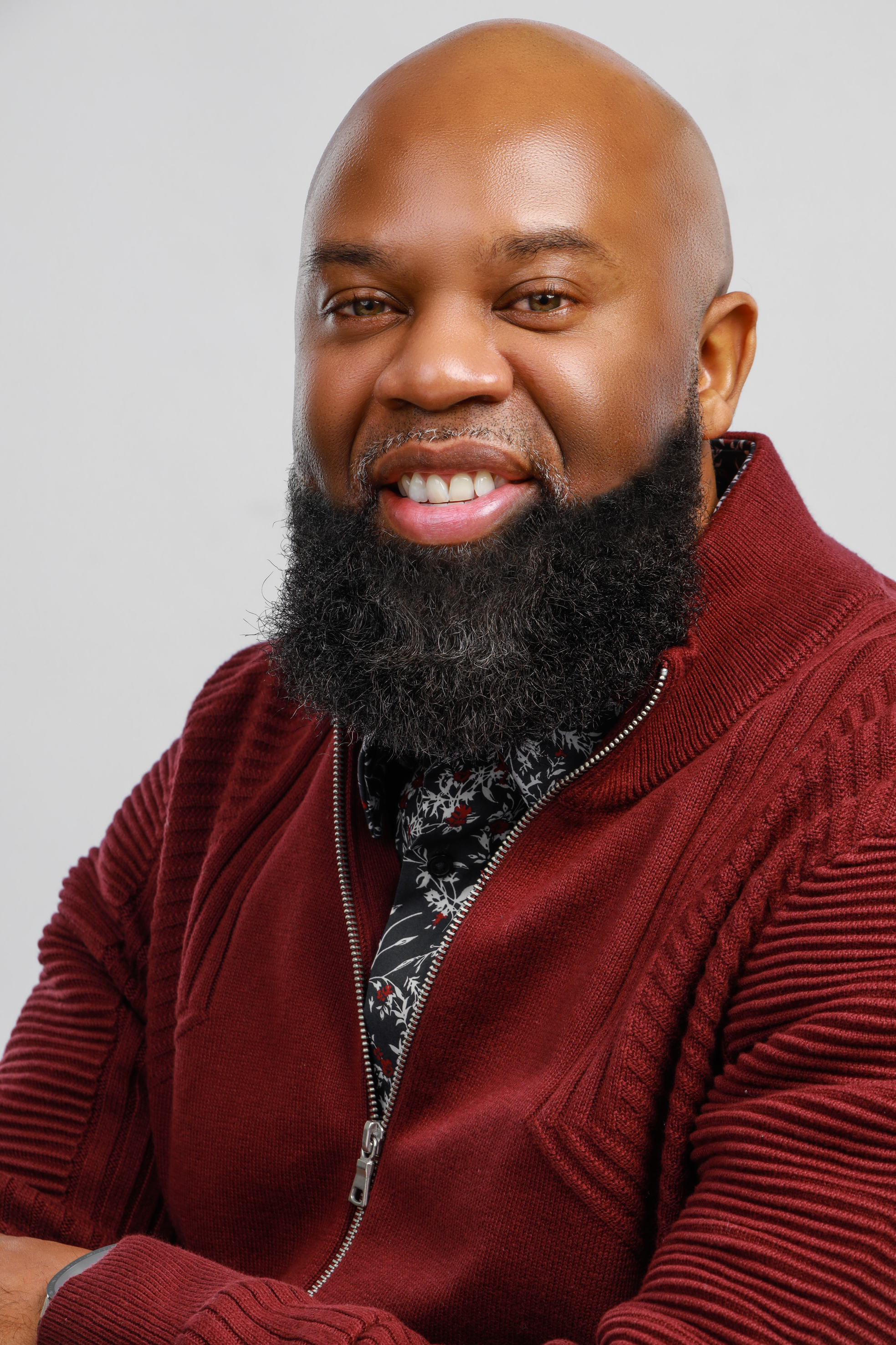 Bald African American man with a beard, wearing a nice smile and a maroon zip-up cardigan sweater