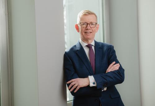 Keith Webster of Carnegie Mellon University, smiling and standing with arms crossed in a suit and purple tie.