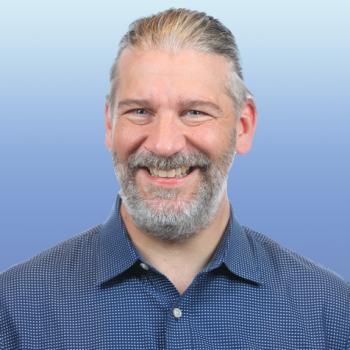 Man with a salt and pepper beard smiling, wearing a dark blue collared shirt.