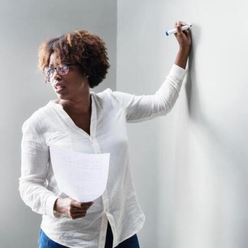 African American woman wearing a white collared shirt, holding a marker at a White Board